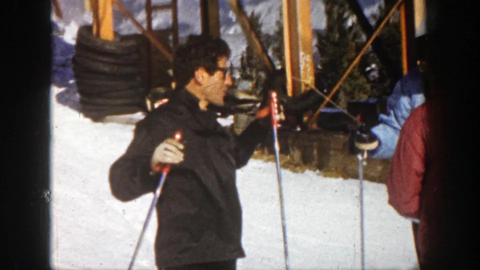 Aspen ski-resort scene with a man holding poles and other skiers waiting beside a wooden lift structure.