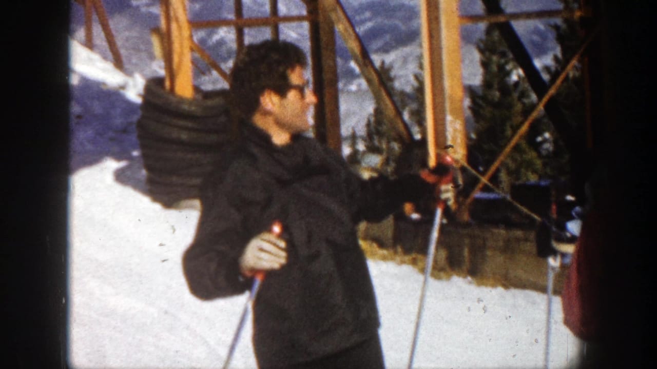 Man with ski poles turns on a snowy slope beside wooden supports and trees.