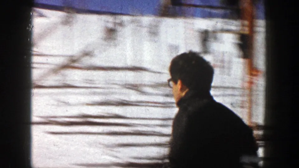A man in dark winter clothing passes close to the camera beside a snowy Aspen ski area, seen in soft 1961 8mm home-movie focus.