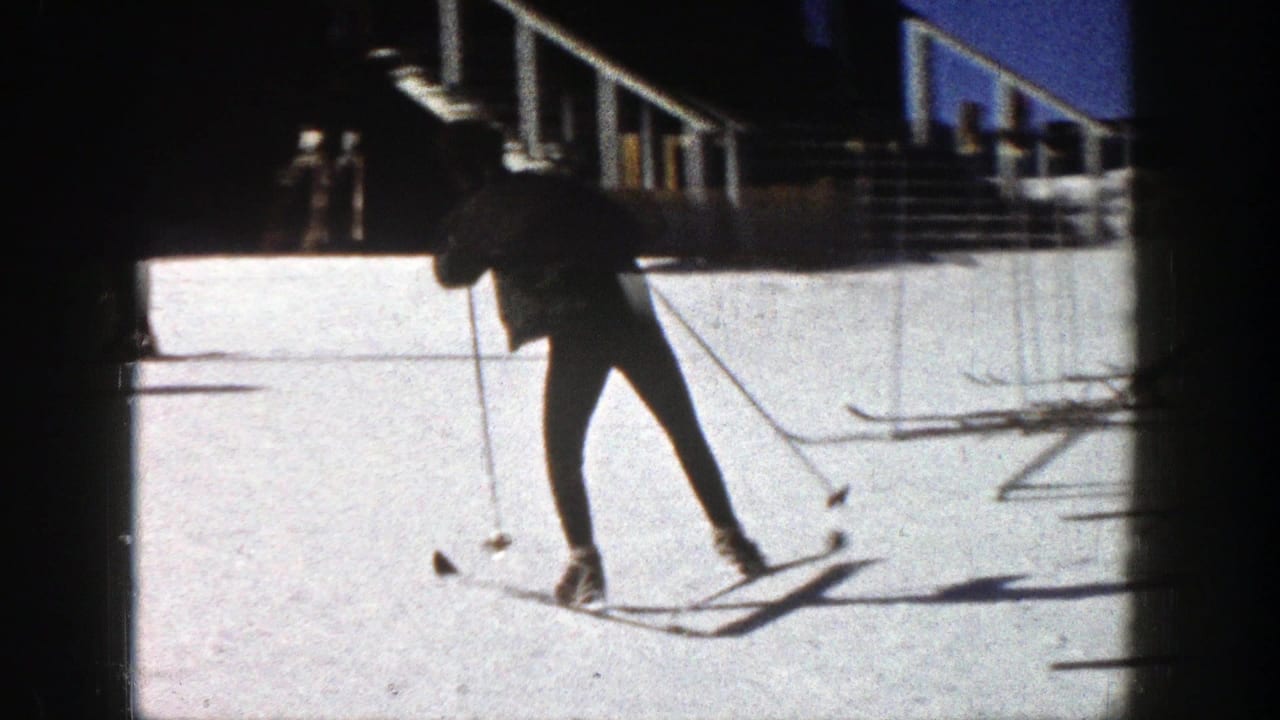 A skier in dark clothing practices with poles on a sunlit Aspen slope, with railings and a building edge in the background.