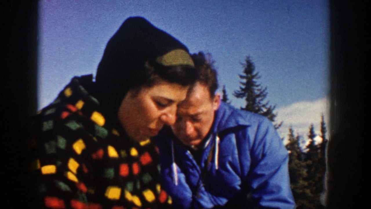 A woman in a patterned hooded coat leans close to a man in a blue puffer jacket outdoors.