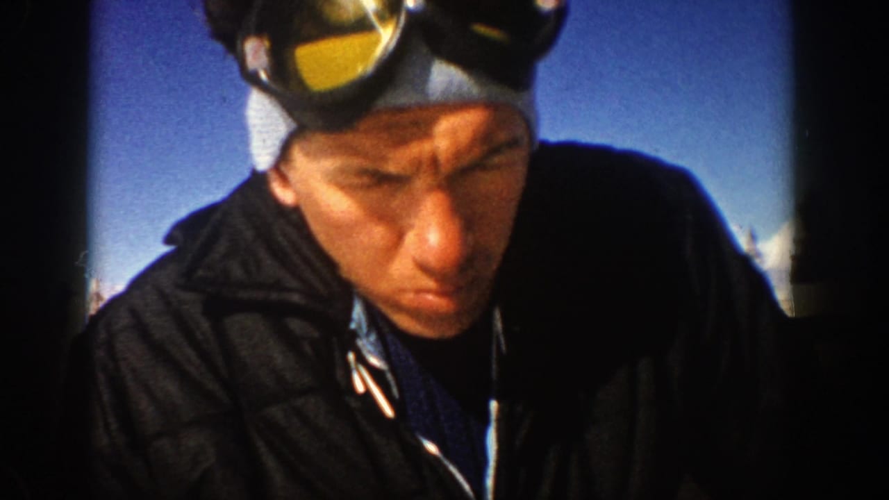 Close view of man in ski goggles and dark jacket looking downward outdoors.