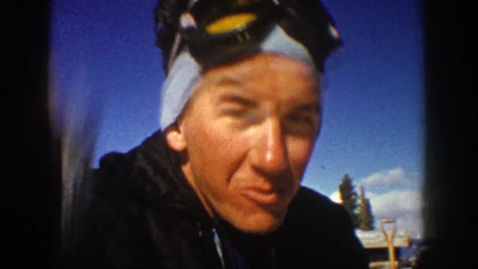 1961 Aspen 8mm frame of a man turning toward the camera in ski gear with snow and trees behind him.