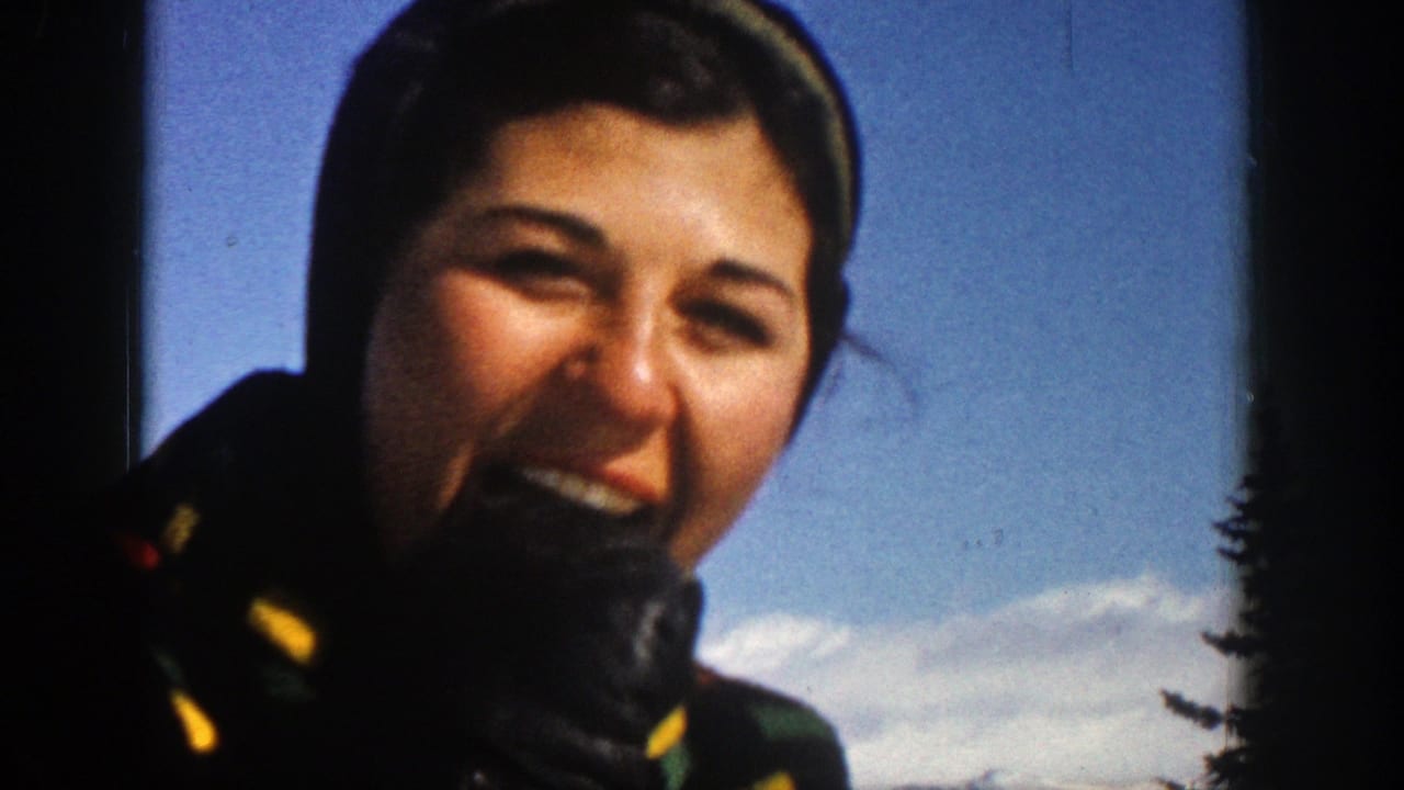 Smiling woman in winter clothing eating snow against blue sky and snowy mountains.