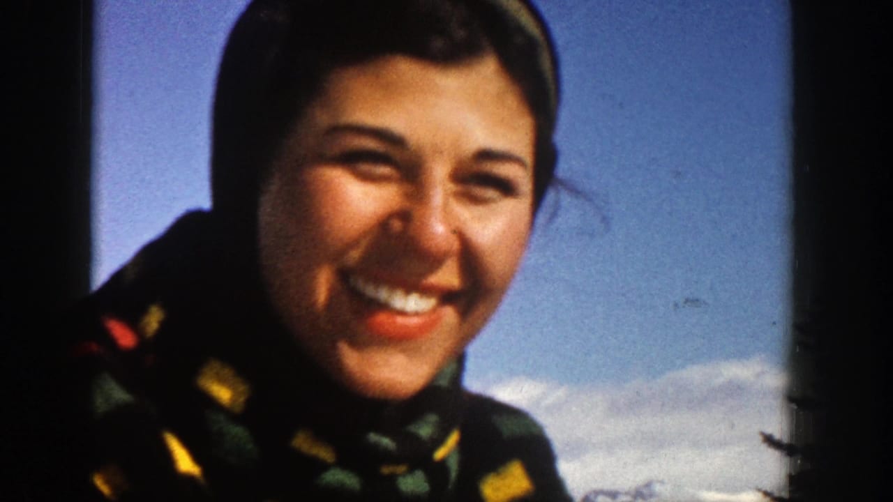 Woman smiling outdoors in winter clothing with snow and blue sky behind her.