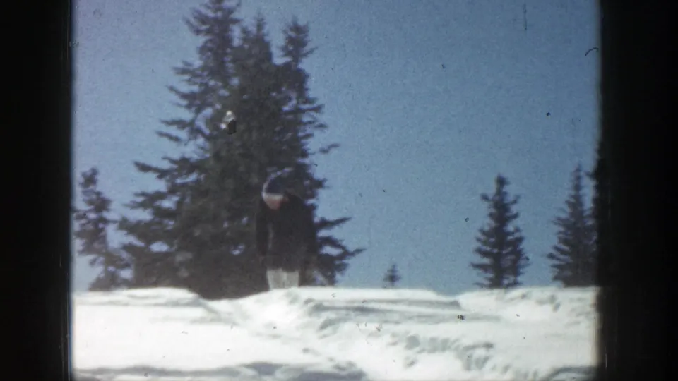 A skier appears at a distance on a snowy Aspen slope, framed by evergreen trees in 1961 8mm footage.