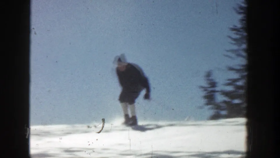 A skier in dark clothing glides across bright snow in metadata-supported 1961 Aspen home-movie footage.