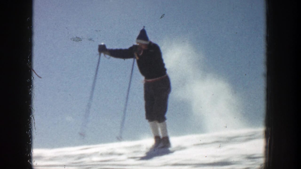 Skier in dark jacket and knit hat gliding on a bright snowy slope.