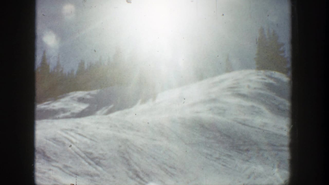1961 Aspen 8mm frame showing a snowy slope, strong sun flare, and evergreen trees beyond the ridge.