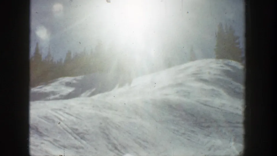 1961 Aspen 8mm frame showing a snowy slope, strong sun flare, and evergreen trees beyond the ridge.