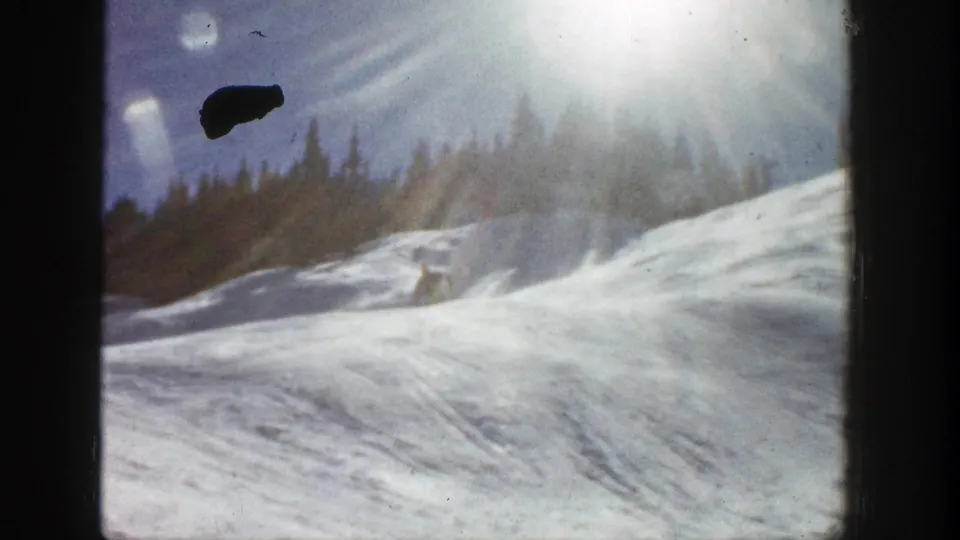 Vintage 8mm Aspen slope frame with bright flare, evergreen background, textured snow, and visible film debris.