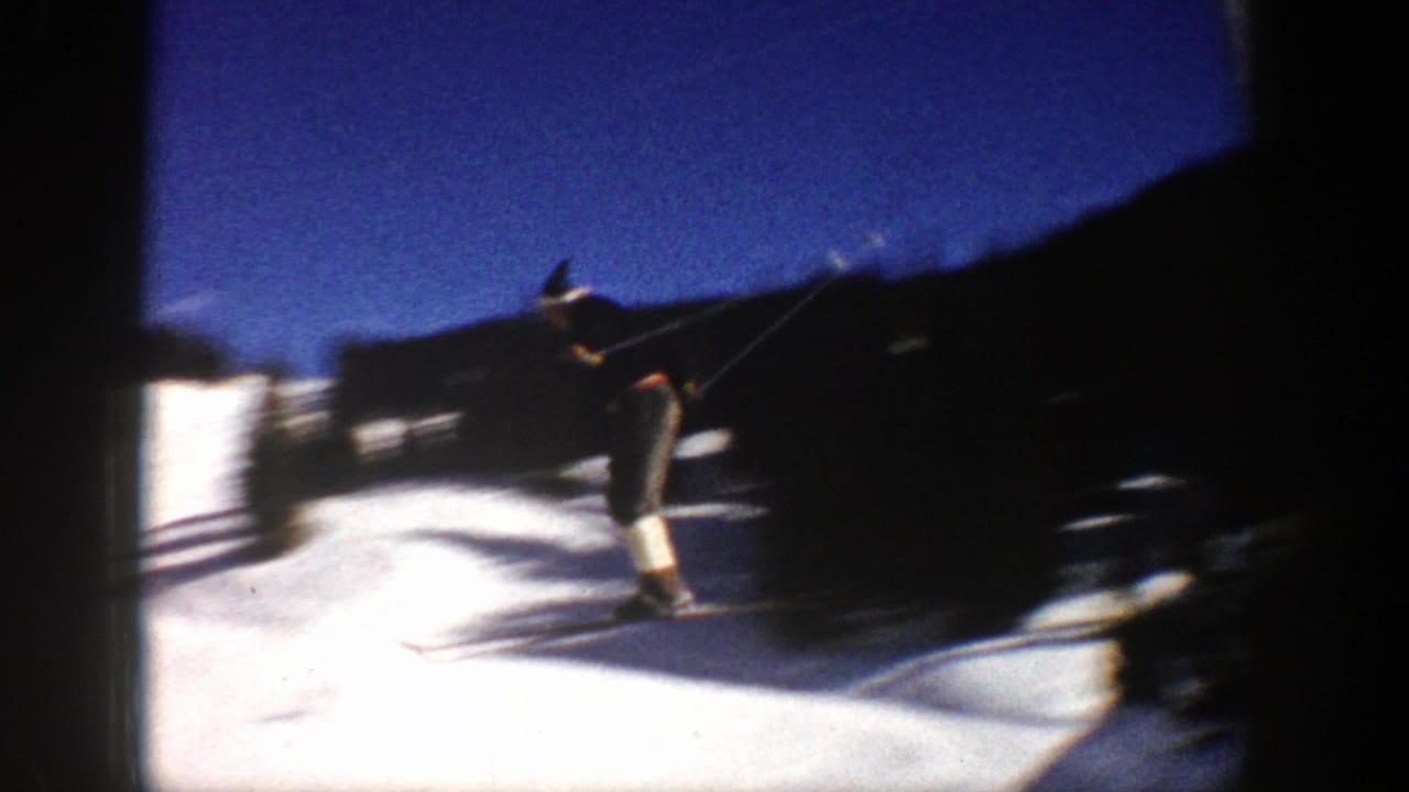 Skier in dark winter clothing moves across bright snow near a shadowed slope edge.