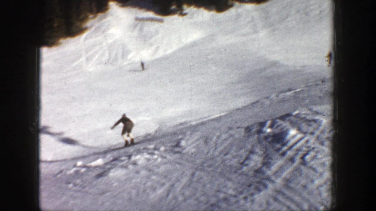 Small skier descends an open snowy slope with tracks and trees near the top edge.