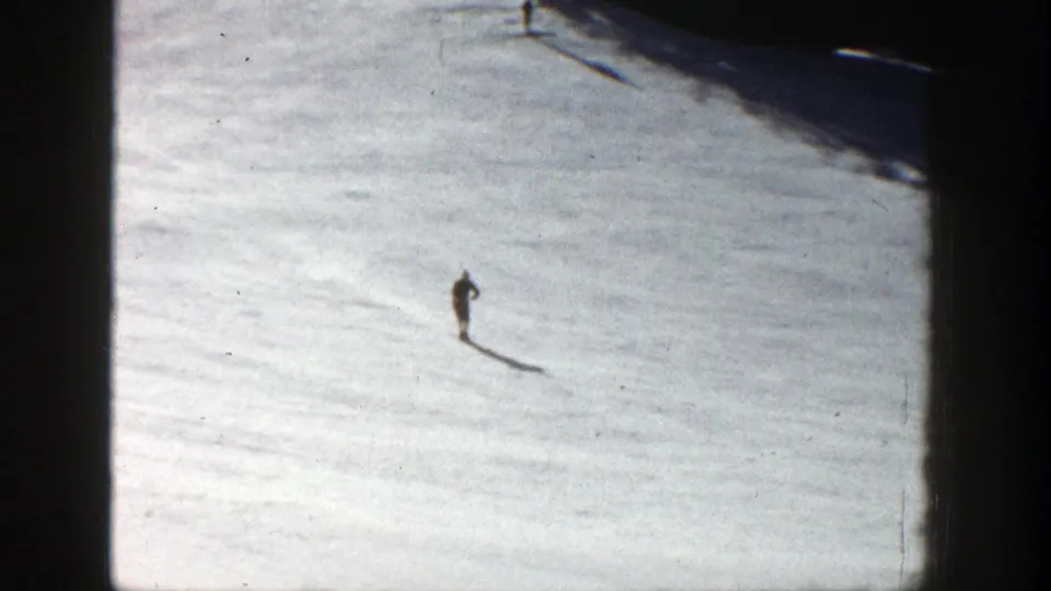 A lone skier crosses the snowy Aspen slope in the 1961 8mm frame, isolated against bright snow with a long shadow.