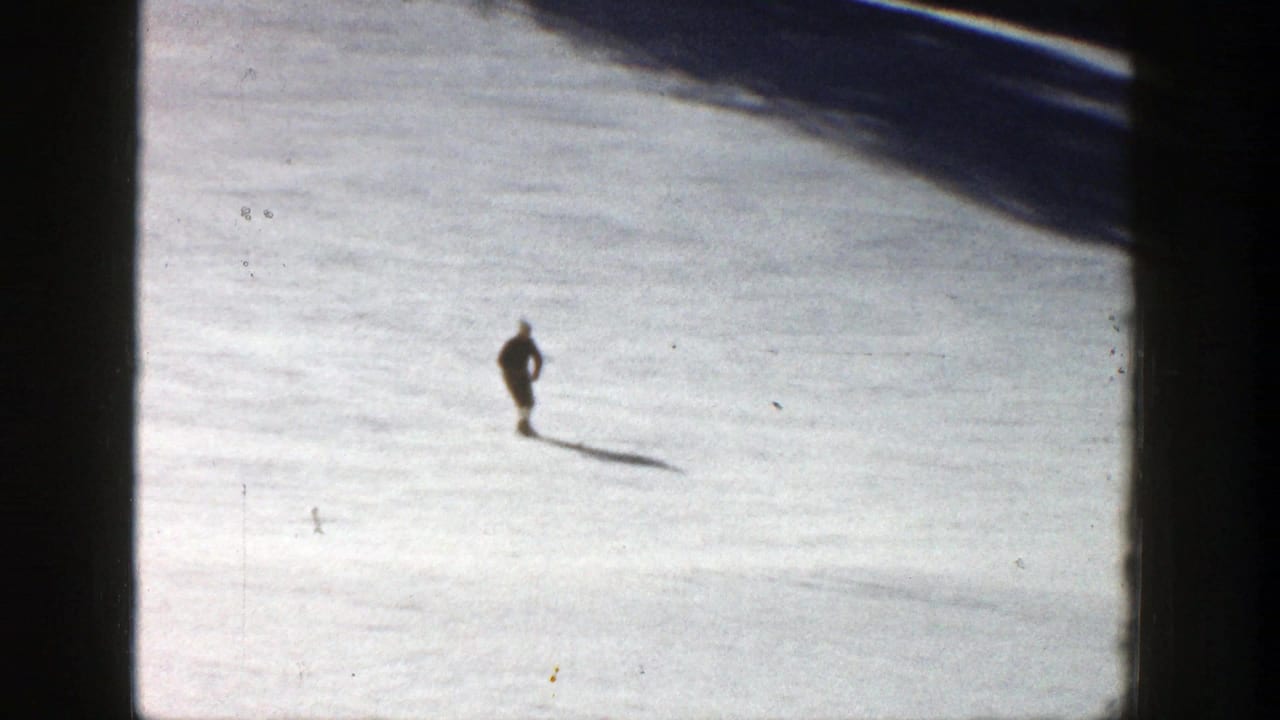 Distant skier gliding across a bright snowy slope with a long shadow.