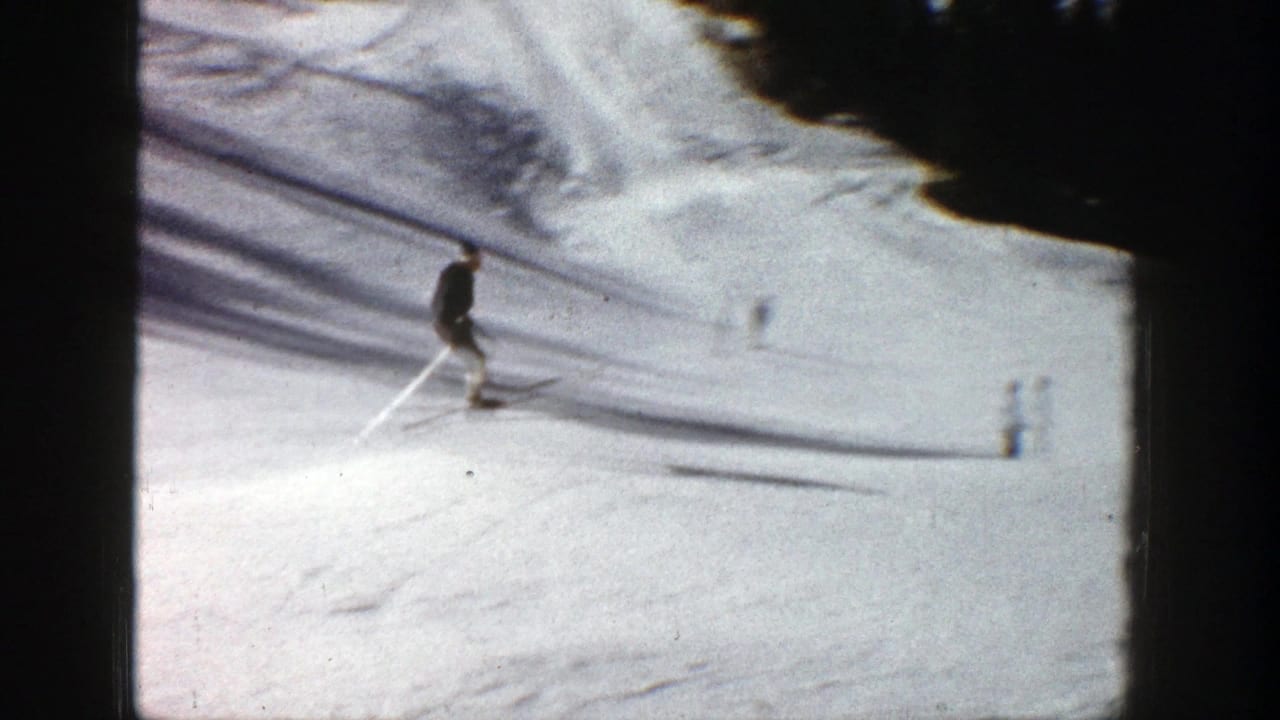Skier in a dark or grey jacket descends an Aspen ski slope, with trees and snow texture visible in 1961 8mm footage.