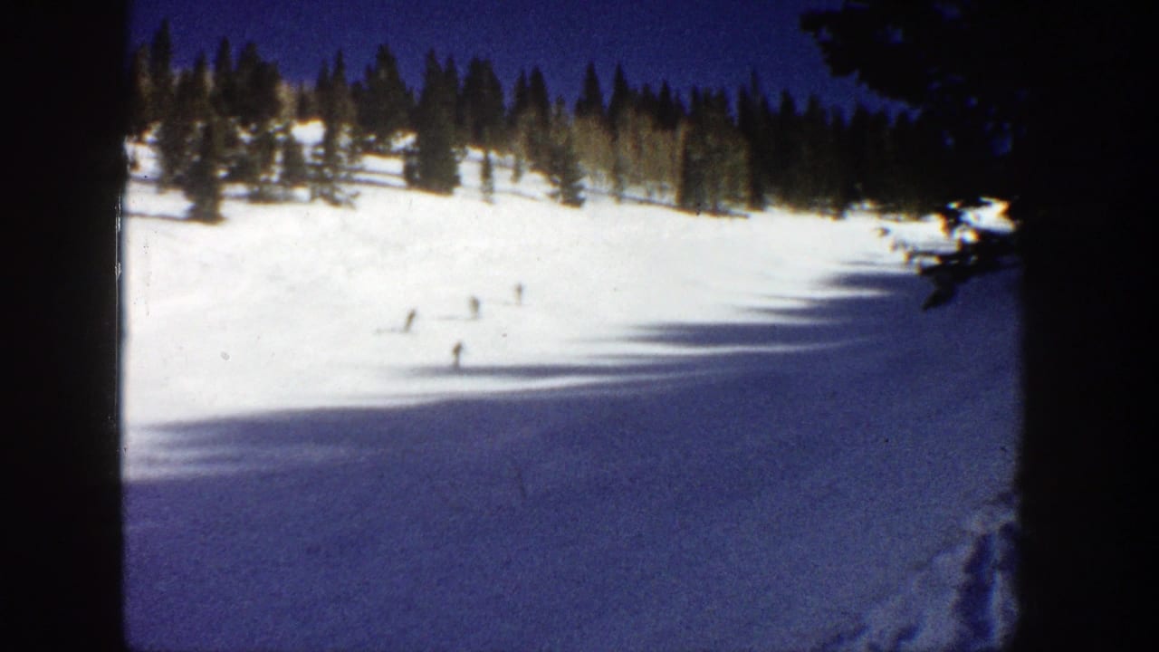 Distant skiers cross a bright Aspen ski run in 1961, with evergreens above and heavy shadow falling across the snow.
