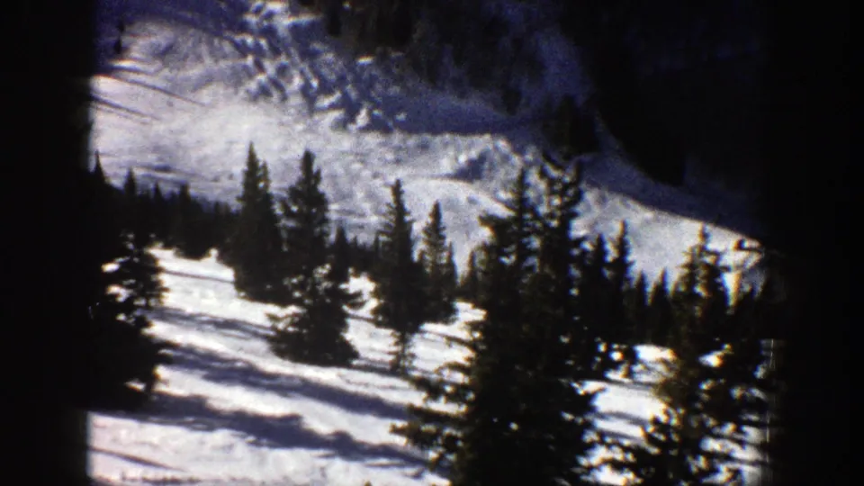 1961 Aspen home-movie frame showing snow-covered mountain terrain, scattered evergreen trees, and high-contrast winter sunlight.