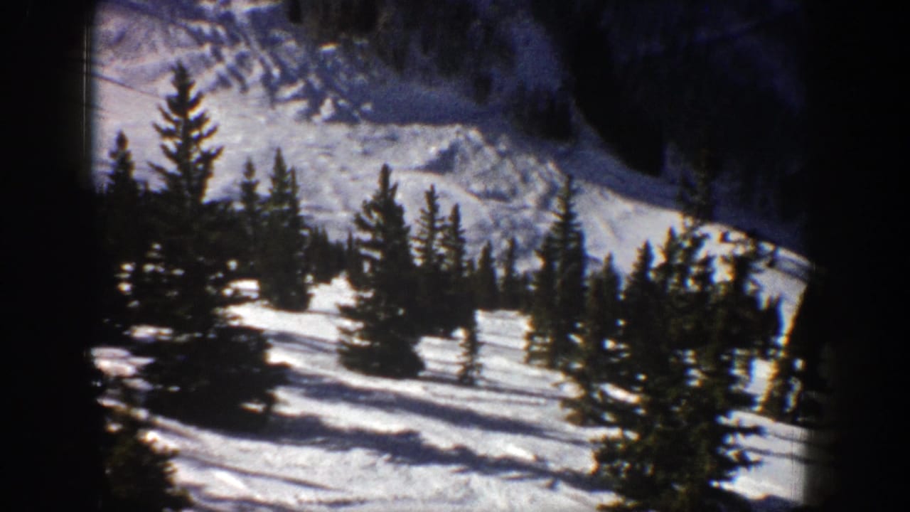 1961 Aspen home-movie frame showing evergreen trees scattered across a snow-covered mountain slope.