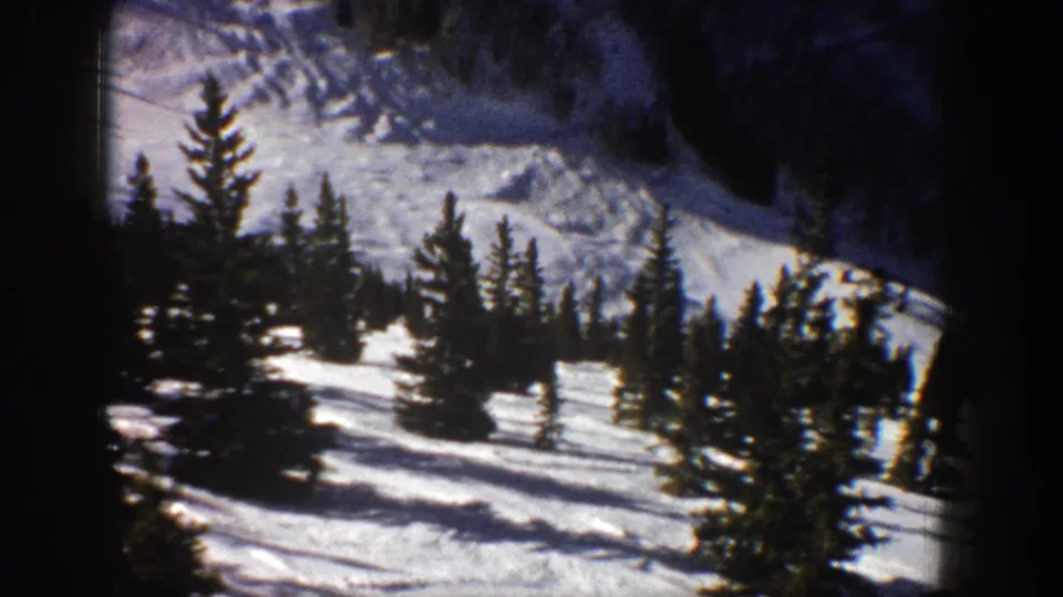 1961 Aspen home-movie frame showing evergreen trees scattered across a snow-covered mountain slope.