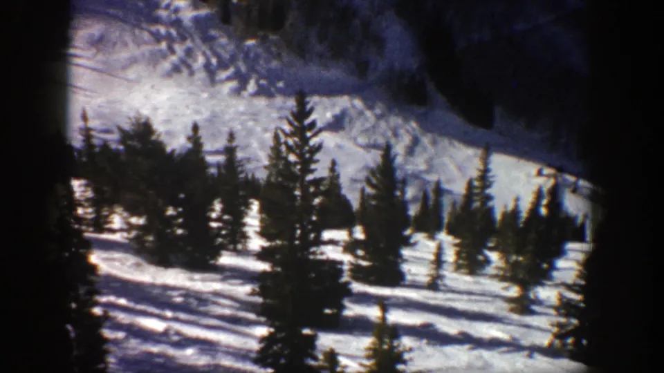 Vintage 8mm frame from Aspen showing scattered evergreens and long shadows across a snowy slope.