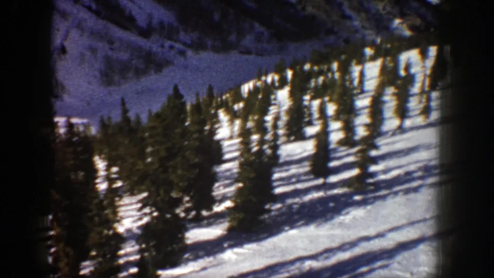 Vintage 8mm frame of a snowy Aspen hillside with dark evergreens, long shadows, and visible film-frame borders.