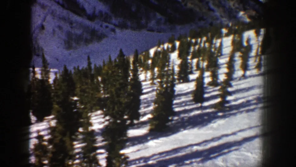 1961 Aspen, Colorado frame showing a snow-covered slope dotted with evergreens under bright daylight.