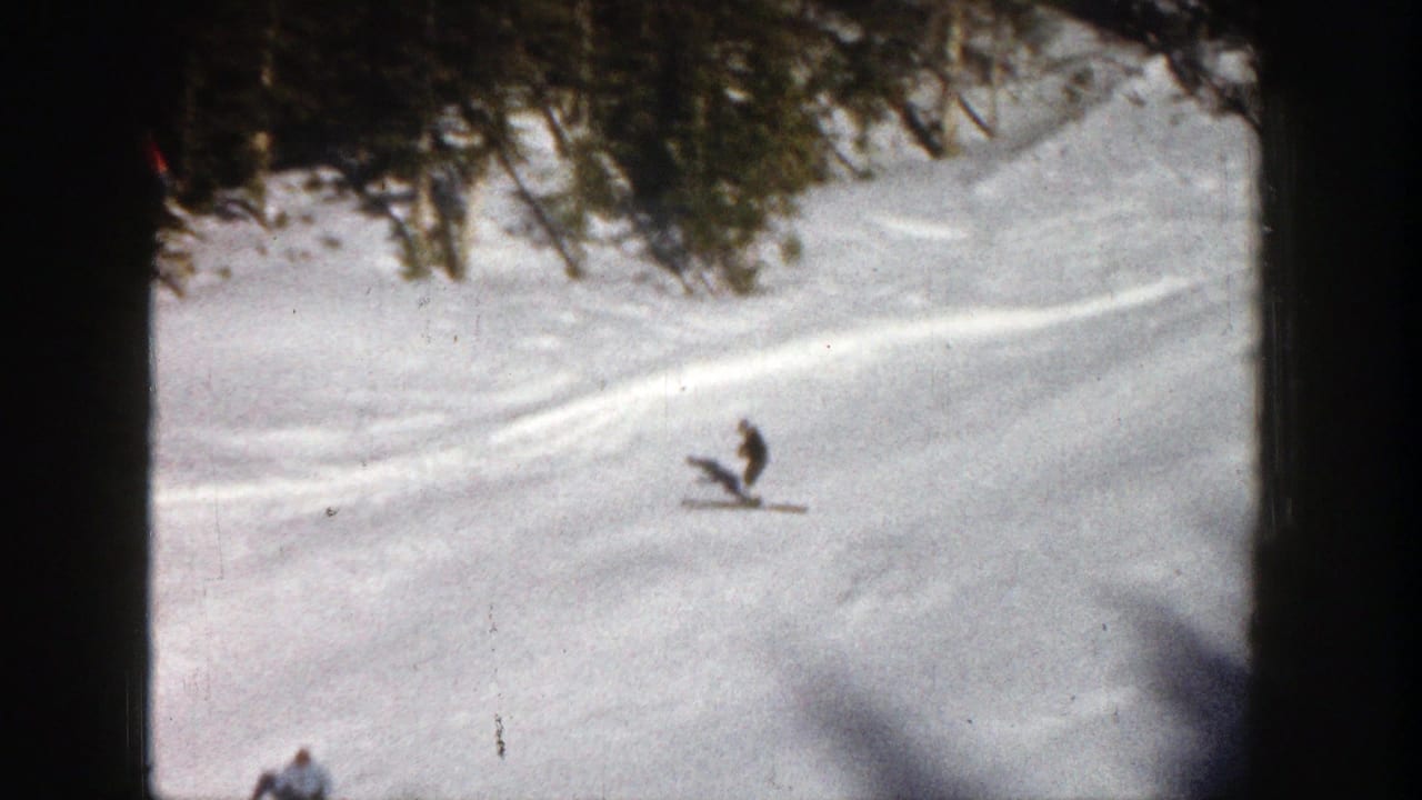 A distant skier crosses a snowy Aspen slope in 1961 home-movie footage, with evergreen trees and visible ski marks behind.