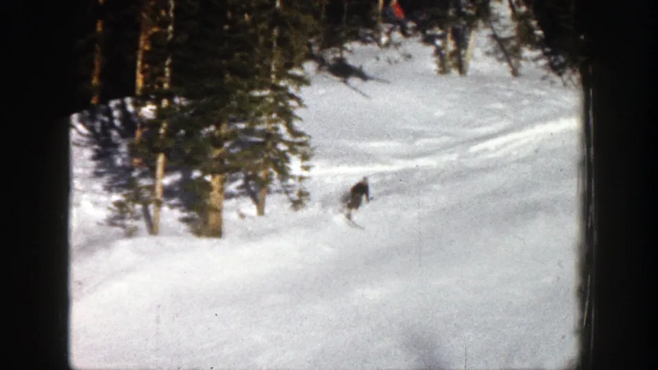 1961 Aspen ski footage shows a small figure descending near evergreen trees on a snow-covered run.