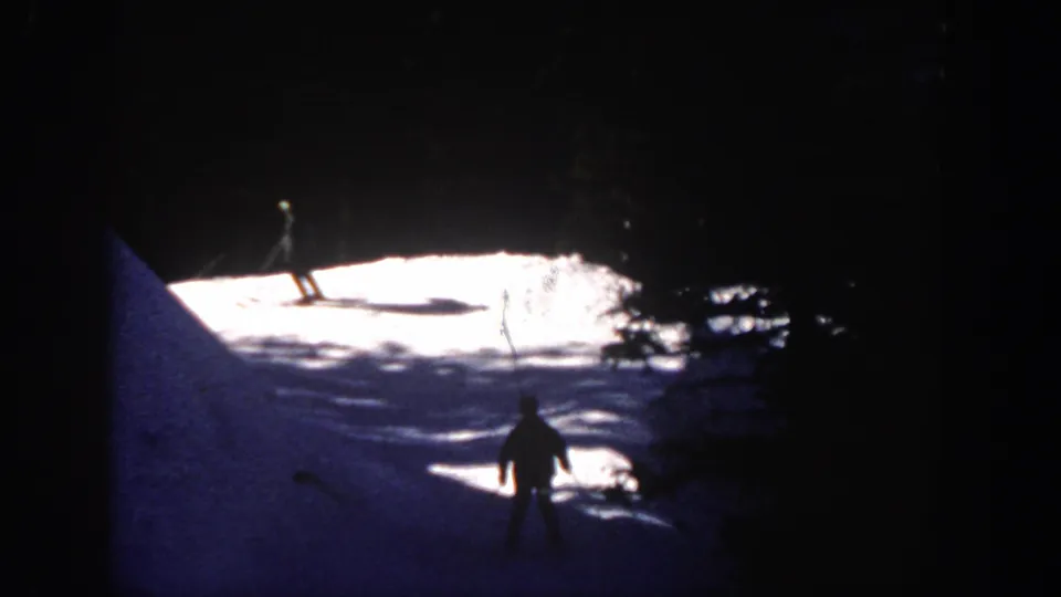 A distant skier in Aspen, Colorado, 1961, moves across a sunlit snow patch with dark forest framing the slope.