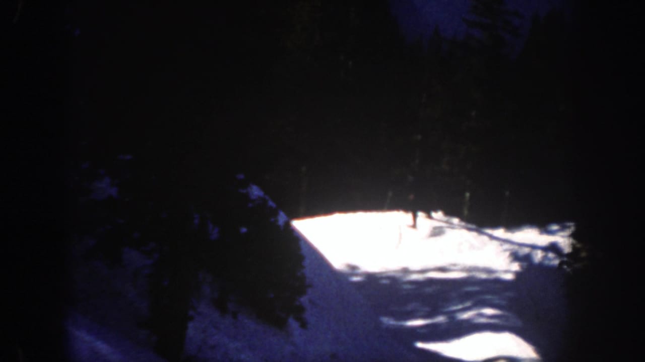 Dark, underexposed 8mm frame of a snowy Aspen slope, trees, and bright mountain light in the 1961 home-movie sequence.
