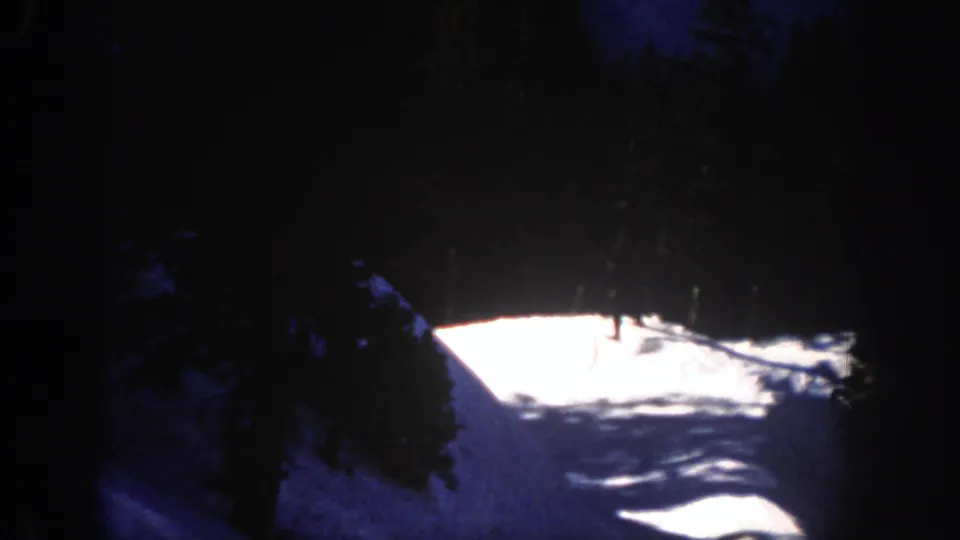 Dark, underexposed 8mm frame of a snowy Aspen slope, trees, and bright mountain light in the 1961 home-movie sequence.