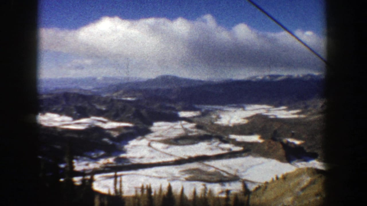 Snowy mountain valley seen from a high ski-area overlook with lift cable crossing the frame.