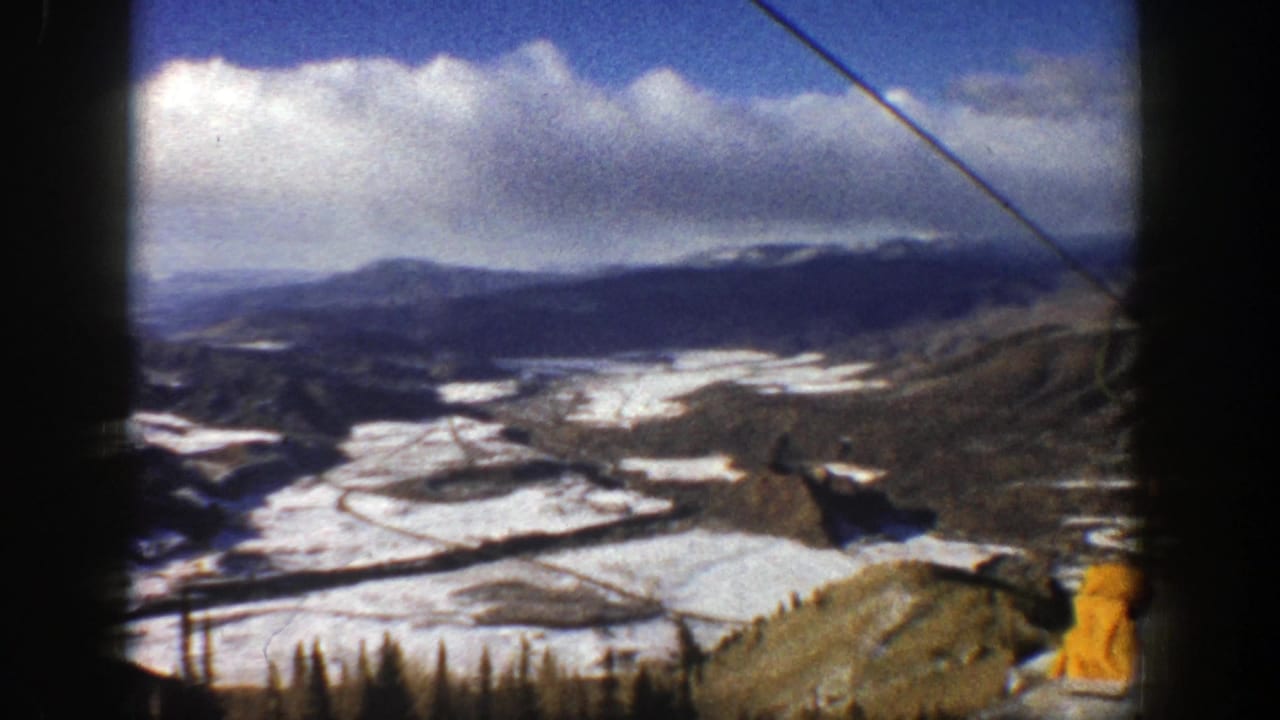 Wide snowy mountain resort view with a lift cable slanting across the sky.
