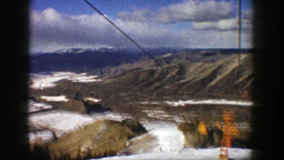 High Aspen resort view from 1961 with snow-covered slope, lift cable, distant mountains, and small figures or skiers far below.