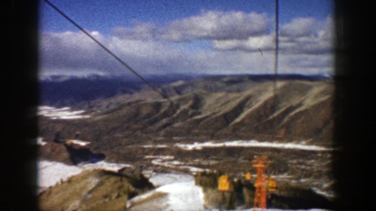 Snow-dusted mountain valley seen from a ski lift with blue sky and clouds.