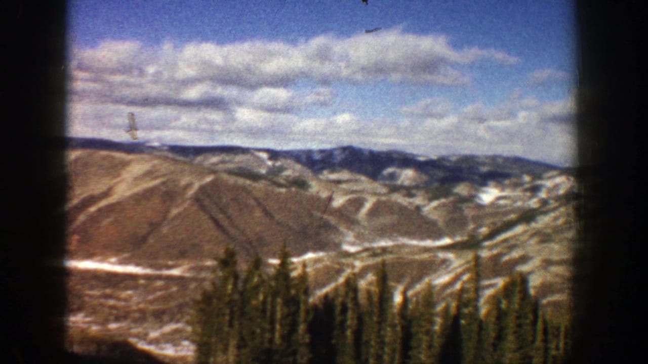 1961 Aspen-area home-movie view of snow-streaked mountain slopes, distant ridges, clouds, and dark evergreen trees.