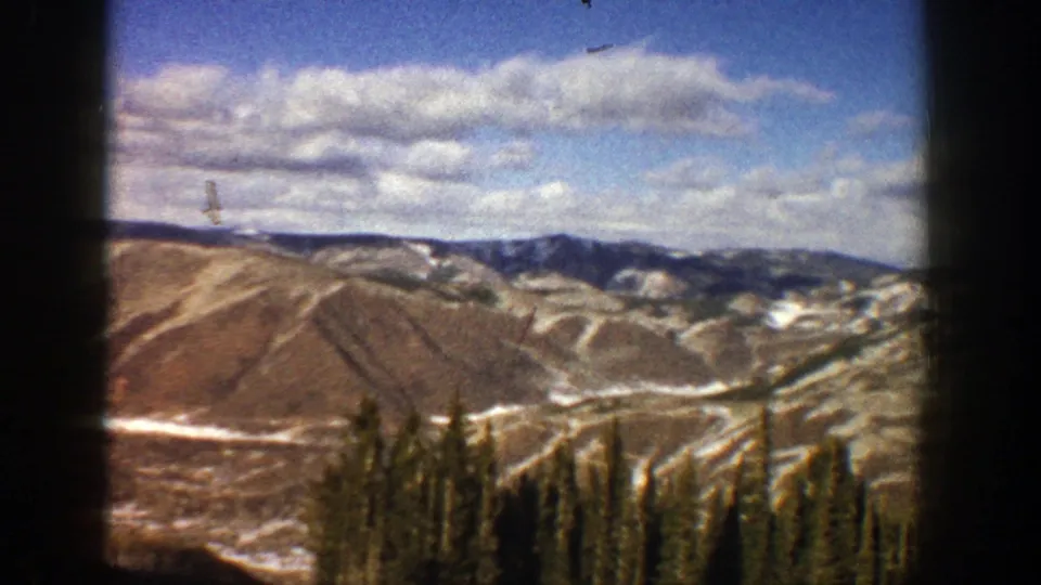 1961 Aspen-area home-movie view of snow-streaked mountain slopes, distant ridges, clouds, and dark evergreen trees.