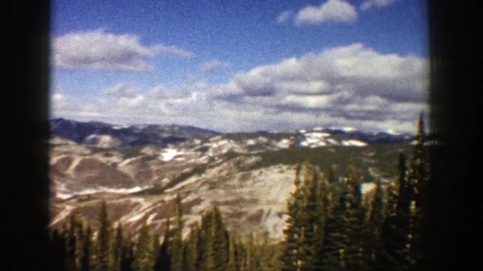 Wide 1961 Aspen mountain view showing snow patches across rolling terrain, dark evergreen trees, and layered clouds.