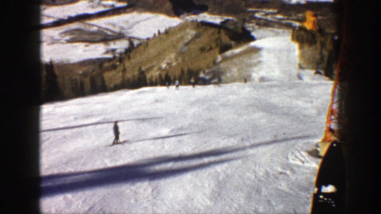 A skier crosses a sunlit snowy slope beneath chairlift shadows near a red tower.