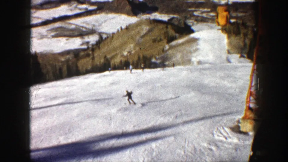 Aspen 1961 ski footage shows a skier descending an open slope, with lift structure and mountain terrain in the background.