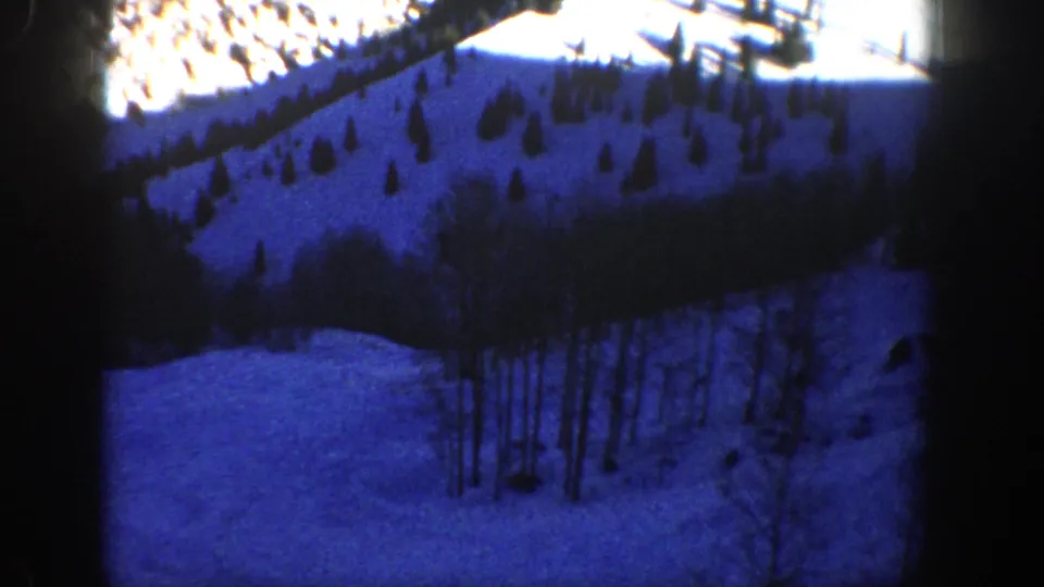 Blue-cast 1961 Aspen, Colorado frame showing a snowy hillside, scattered trees, and darker wooded patches.