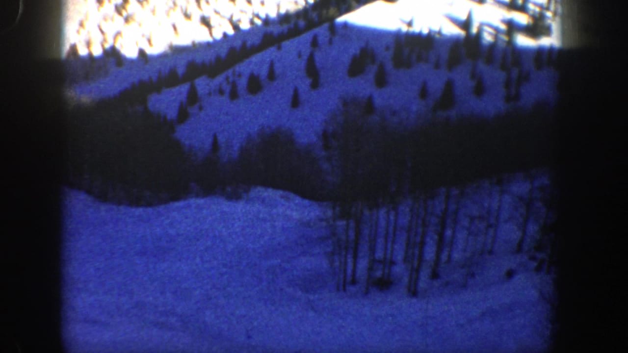 1961 Aspen home-movie frame showing a blue-tinted snow-covered slope with scattered trees and dark 8mm frame edges.