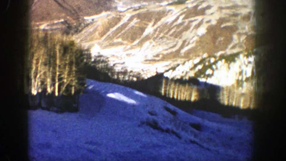 1961 Aspen home-movie frame showing a snow-covered foreground, bare trees, and warmer-toned ridges beyond.