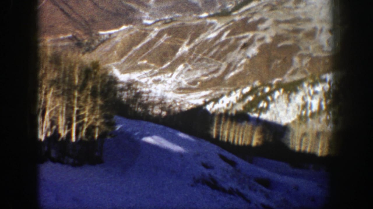 1961 Aspen, Colorado view of a blue-shadowed snowfield, tree line, and pale winter mountains within an 8mm frame.