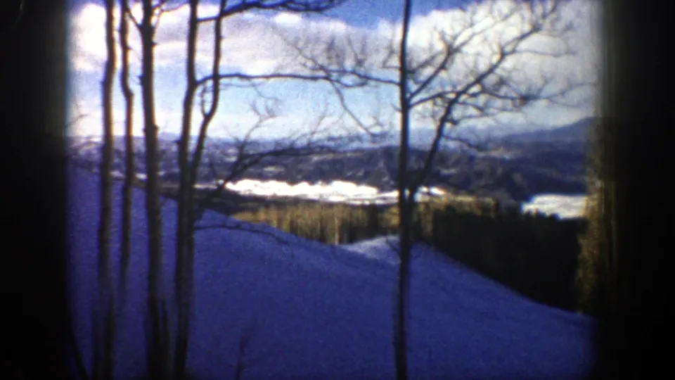 1961 Aspen, Colorado winter landscape with bare aspen trunks, blue snow, and distant mountains under a bright cloudy sky.