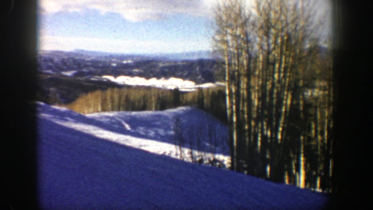 1961 Aspen, Colorado 8mm frame showing a sunlit snow slope, bare aspen trees, and distant winter ridges.