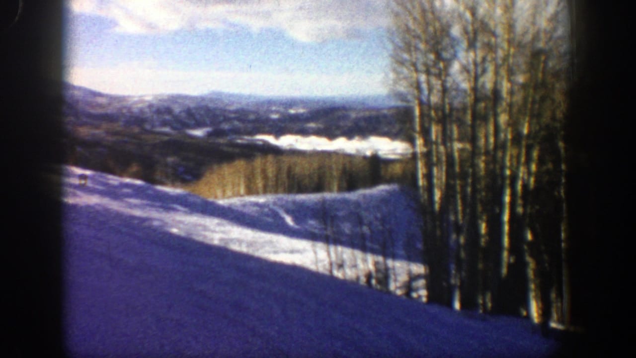 Snowy hill and leafless trees with distant ridges and bright sky.