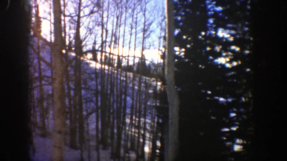 1961 Aspen, Colorado home-movie frame showing bare aspens and dark evergreens against a bright snow-covered mountainside.