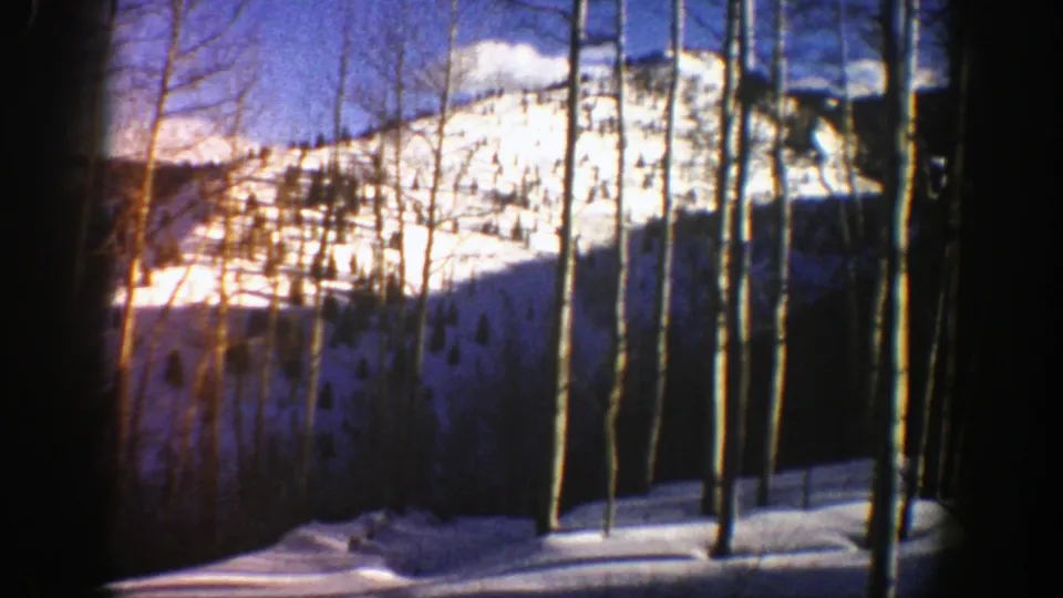1961 Aspen, Colorado winter landscape with a bright snow-covered ridge, slender aspens, evergreens, and visible lens flare.